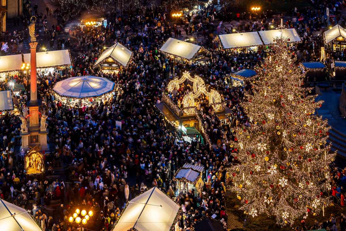 Besucher, Markthütten, ein Karussell und der Weihnachtsbaum auf dem Altstädter Ring nach Einbruch der Dunkelheit.