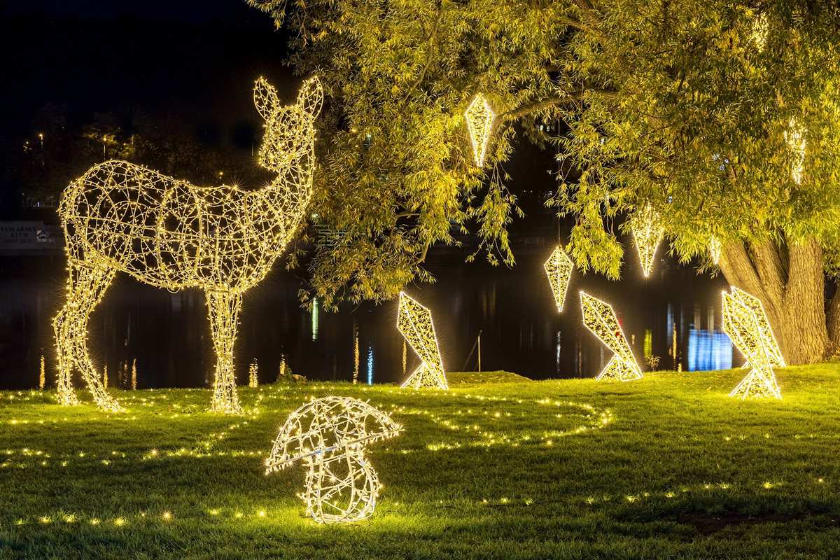 Light sculpture of a deer and mushroom under a tree with hanging light crystals by the river